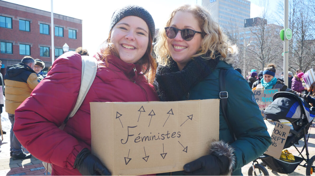 Deux femmes avec une affiches les pointant avec la mention "Féministes"